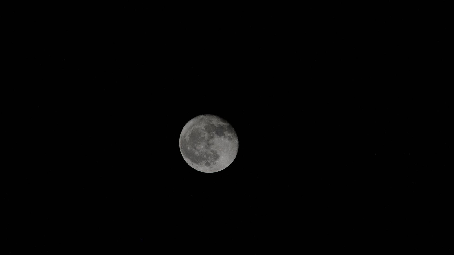 A gibbous moon, slightly less than full, alone in a black sky.